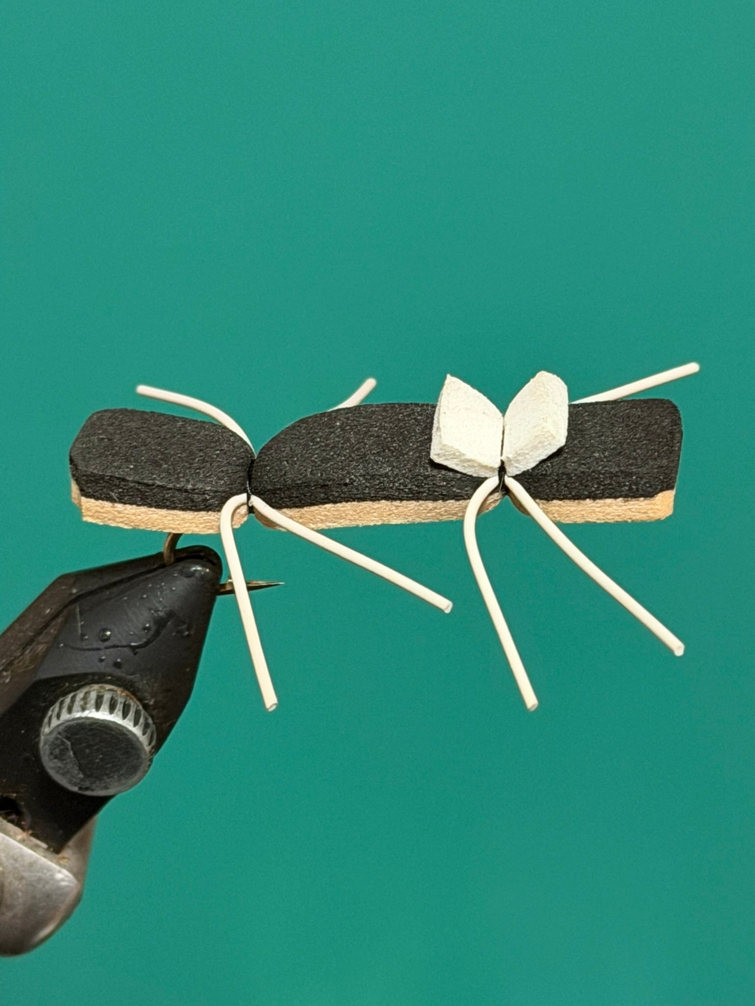 Ant-shaped decorative pin with black body, tan wings, and white leg ties