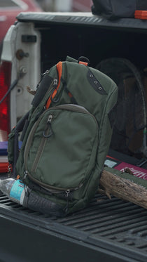 Olive green sling pack with multiple compartments and orange trim, shown in side view
