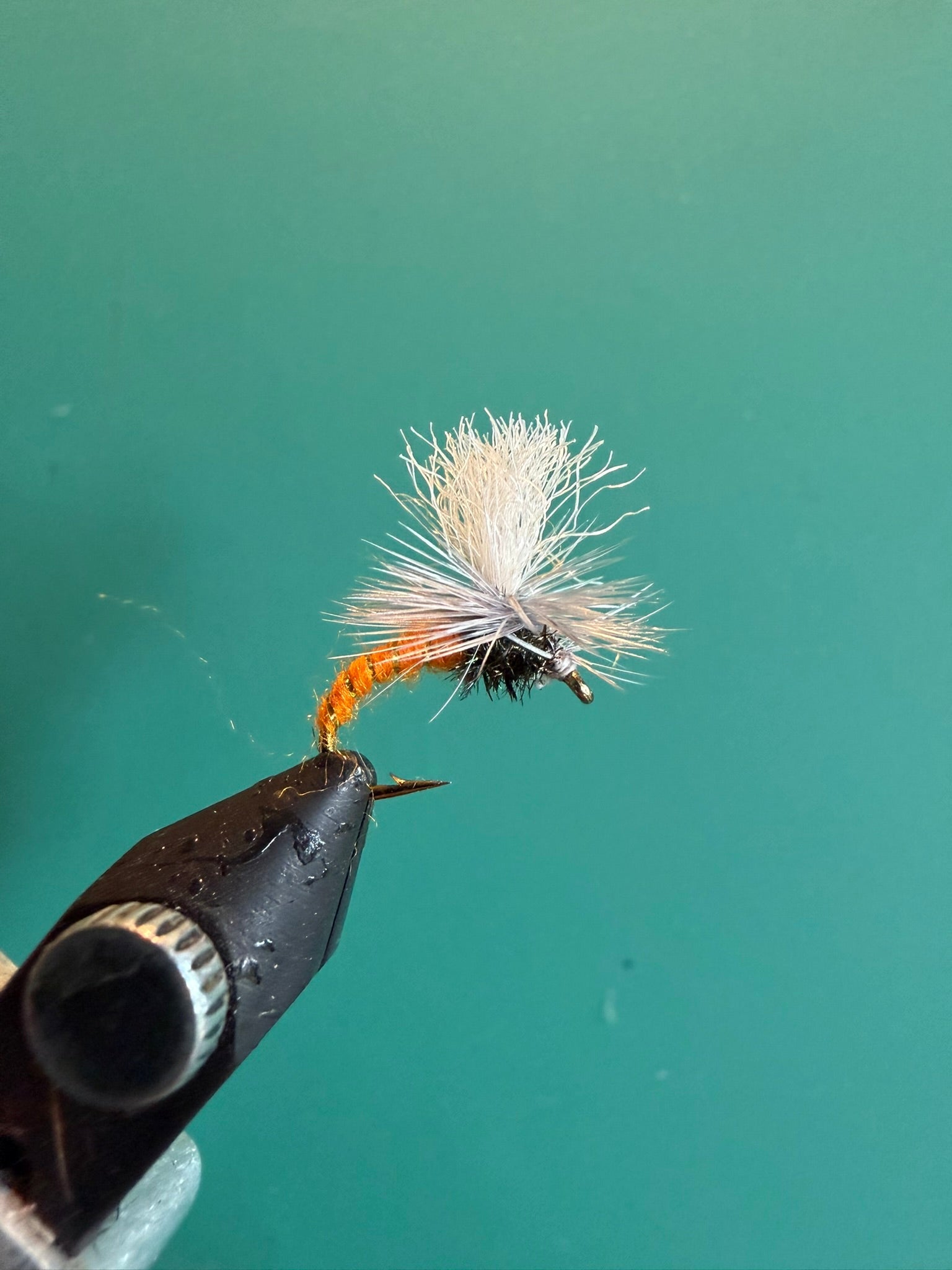 Fishing fly lure with white deer-hair body and orange hackle on barbed hook