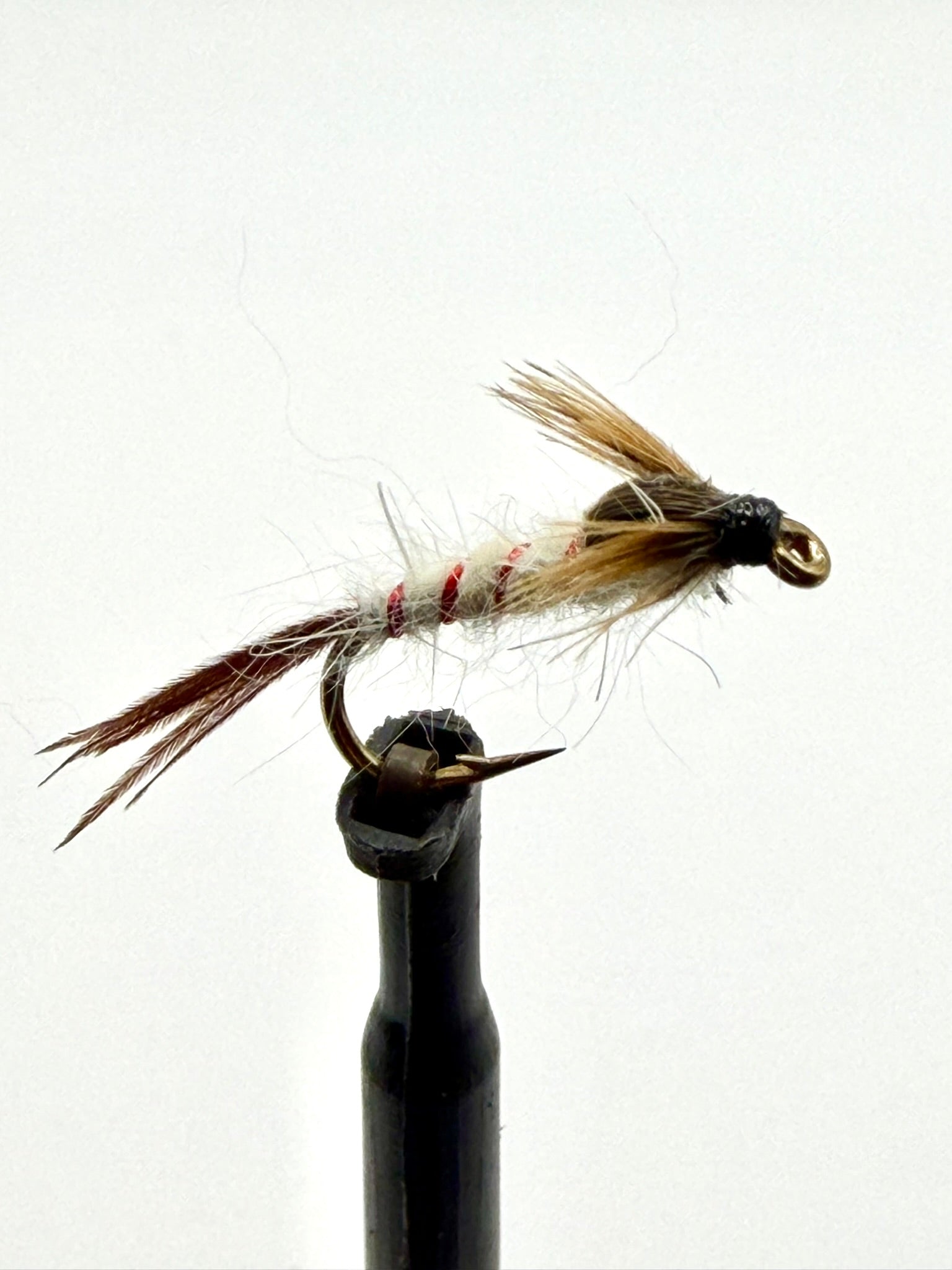 Brown feather fishing fly with red thread accents and gold hook