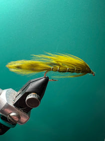 Olive fishing lure with yellow feather tail and two treble hooks