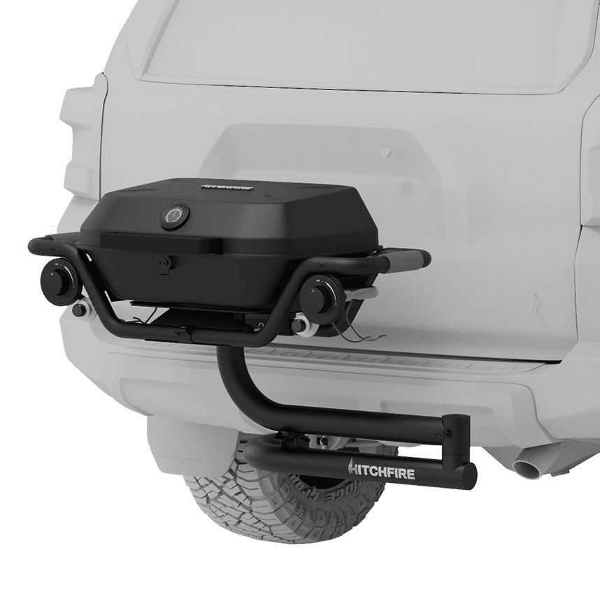 Black hitch-mounted propane grill with lid and side control knobs, mounted on a bumper
