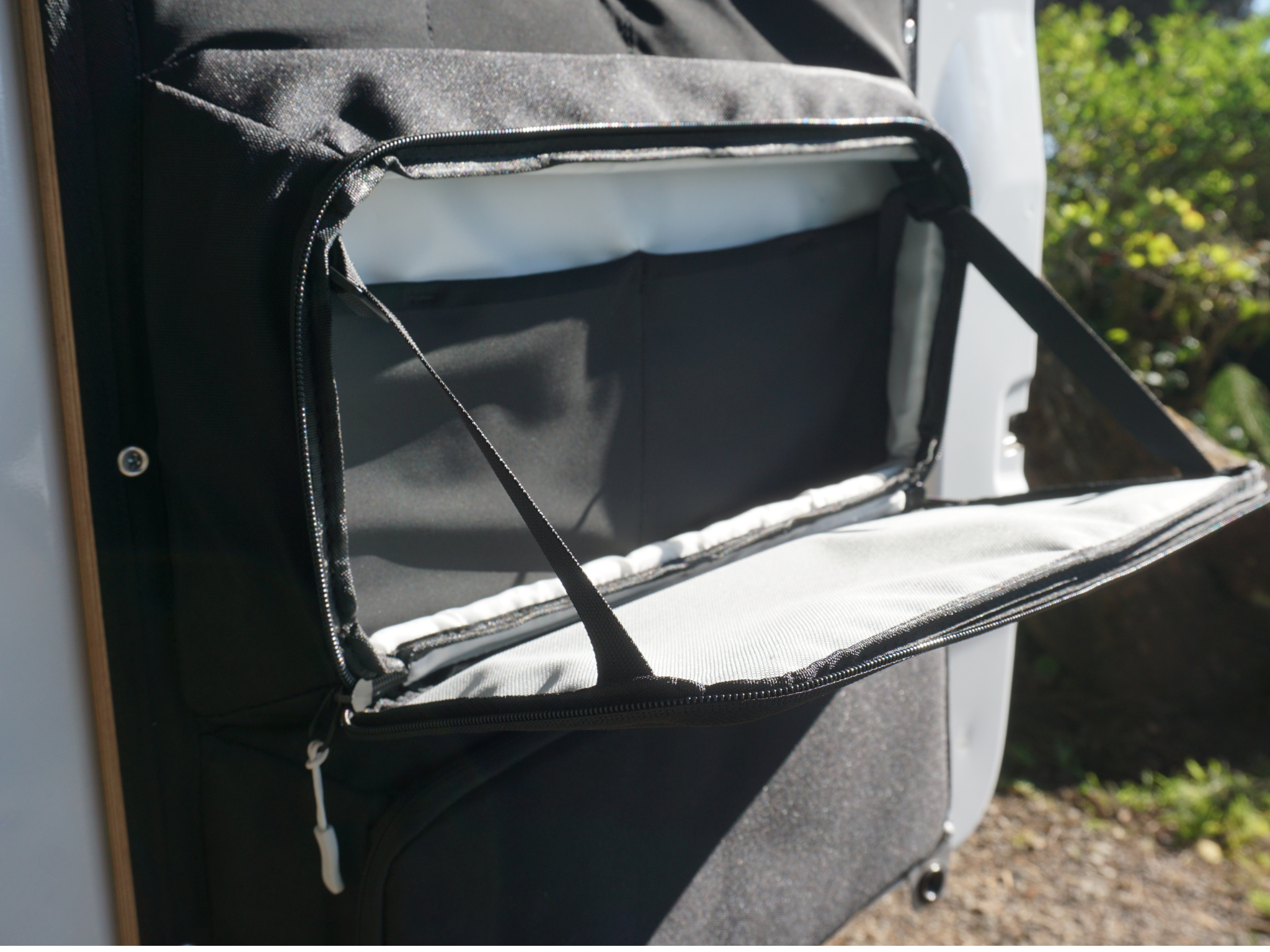 Black open zippered storage compartment on rear door panel with strap and lining
