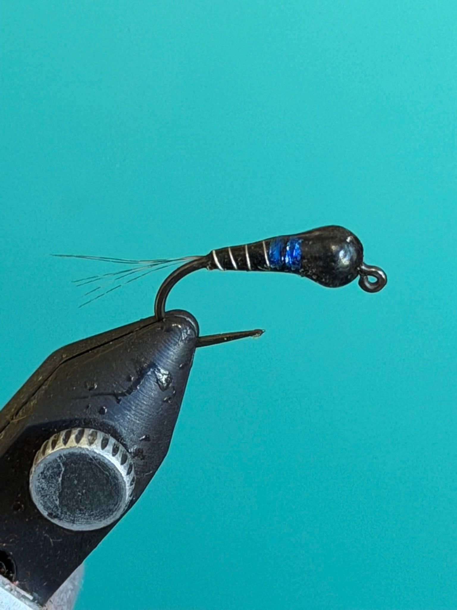 Black and blue fishing lure with feathered tail and curved hook