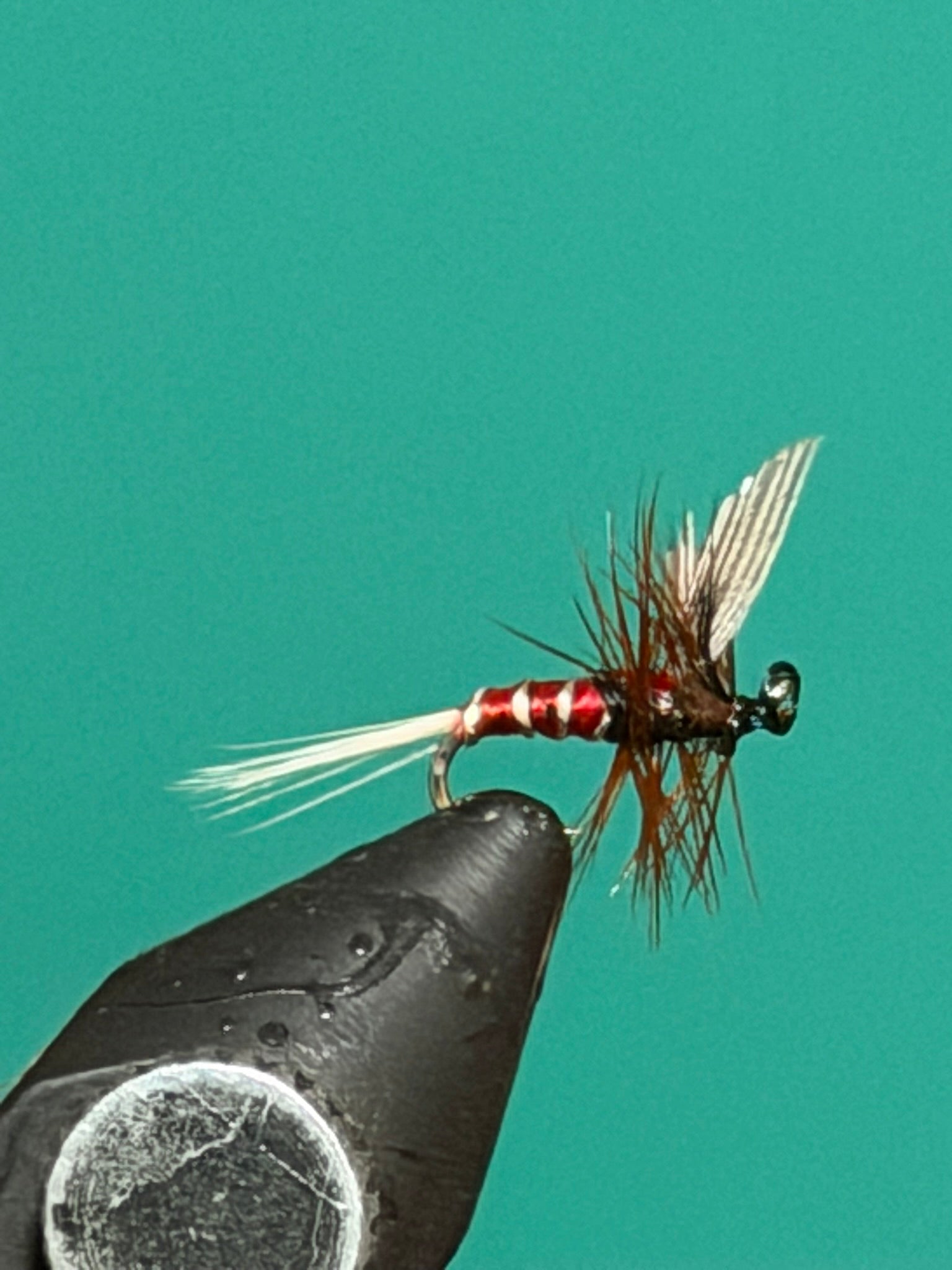 Black fishing spinner lure with red bead, wire body, and feather tail