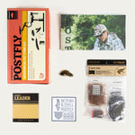 Fly tying kit components laid out in packaging, including leader and hooks materials.