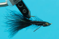 Fishing fly lure, black body with dark tail and gold-rimmed eye