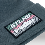 Dark teal knit beanie with ribbed cuff and stitched STLHD logo patch