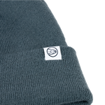 Dark teal knit beanie with ribbed cuff and small circular brand emblem patch