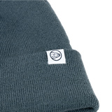 Dark teal knit beanie with ribbed cuff and small circular brand emblem patch