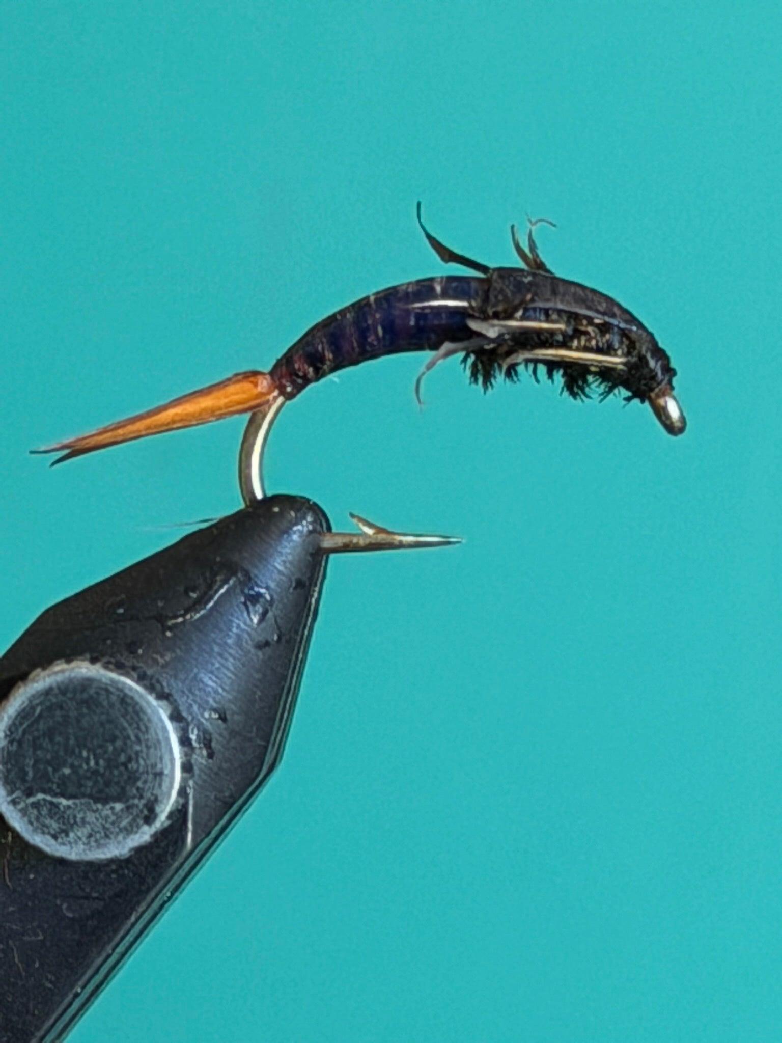 Fishing fly nymph lure: dark black body, orange tail, two metal hooks
