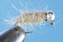 Tungsten jig fly with fuzzy tan body and dark hook, bead head profile